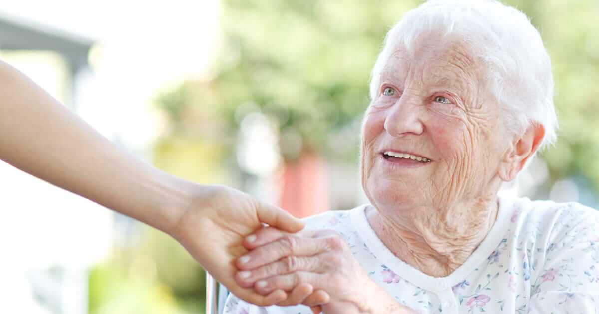 A woman is providing senior care and holding hands with an elderly woman.